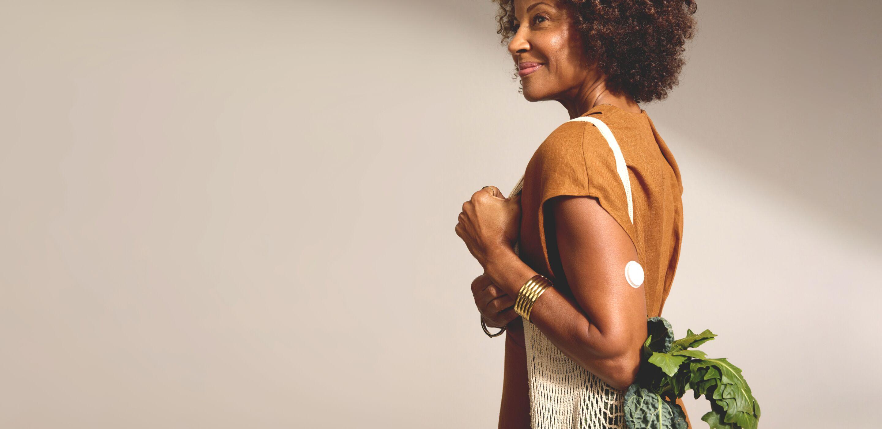 Woman wearing a CGM carrying bag of vegetables. 