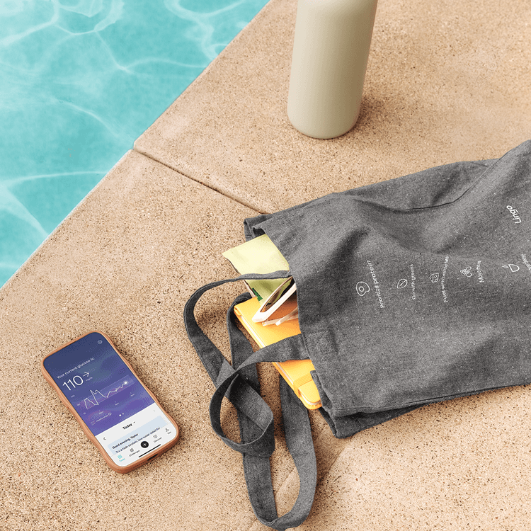 A recycled tote bag, and a phone showing the Lingo application on a pool deck next to sparkling blue water. 