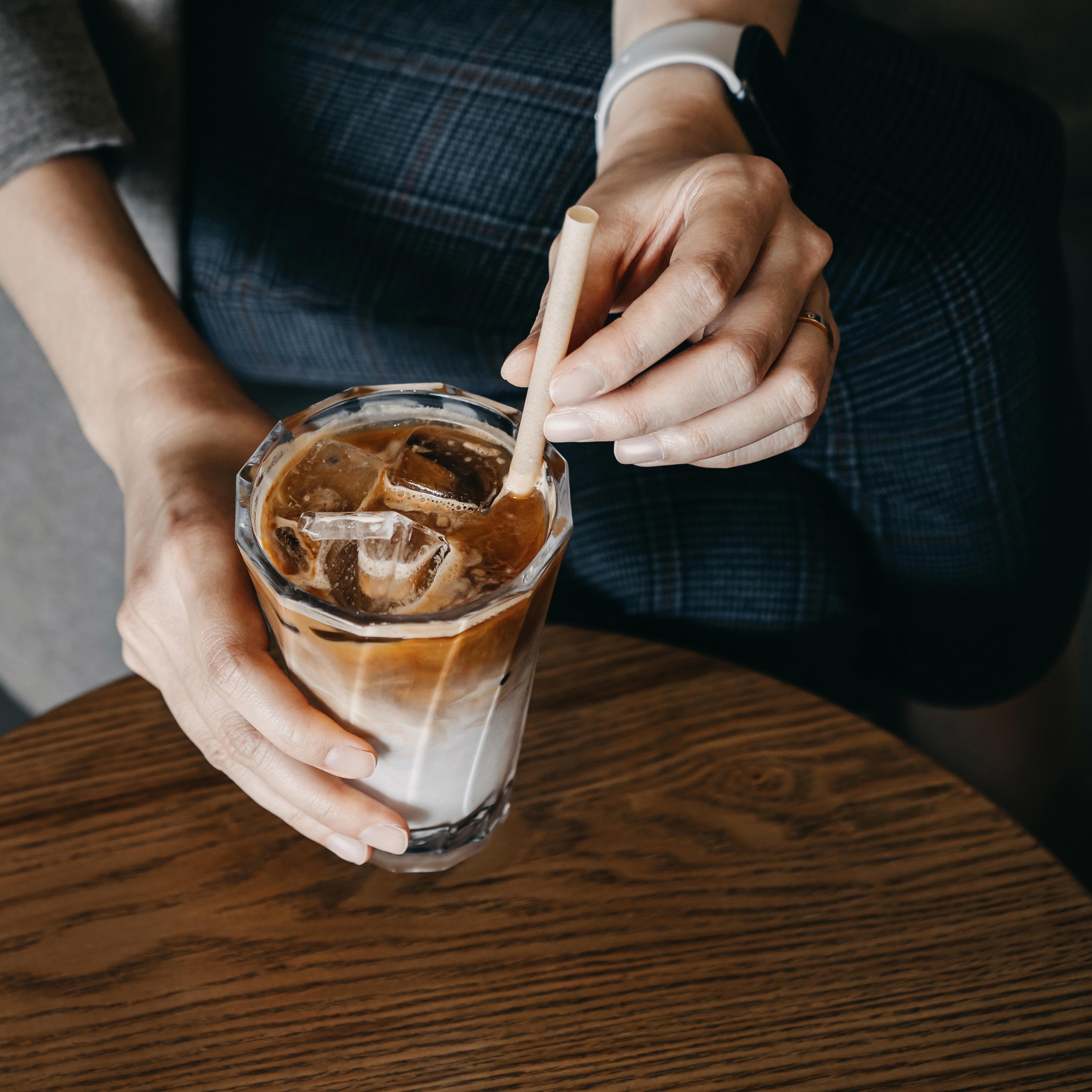 A person holds a glass of iced coffee with a straw. 