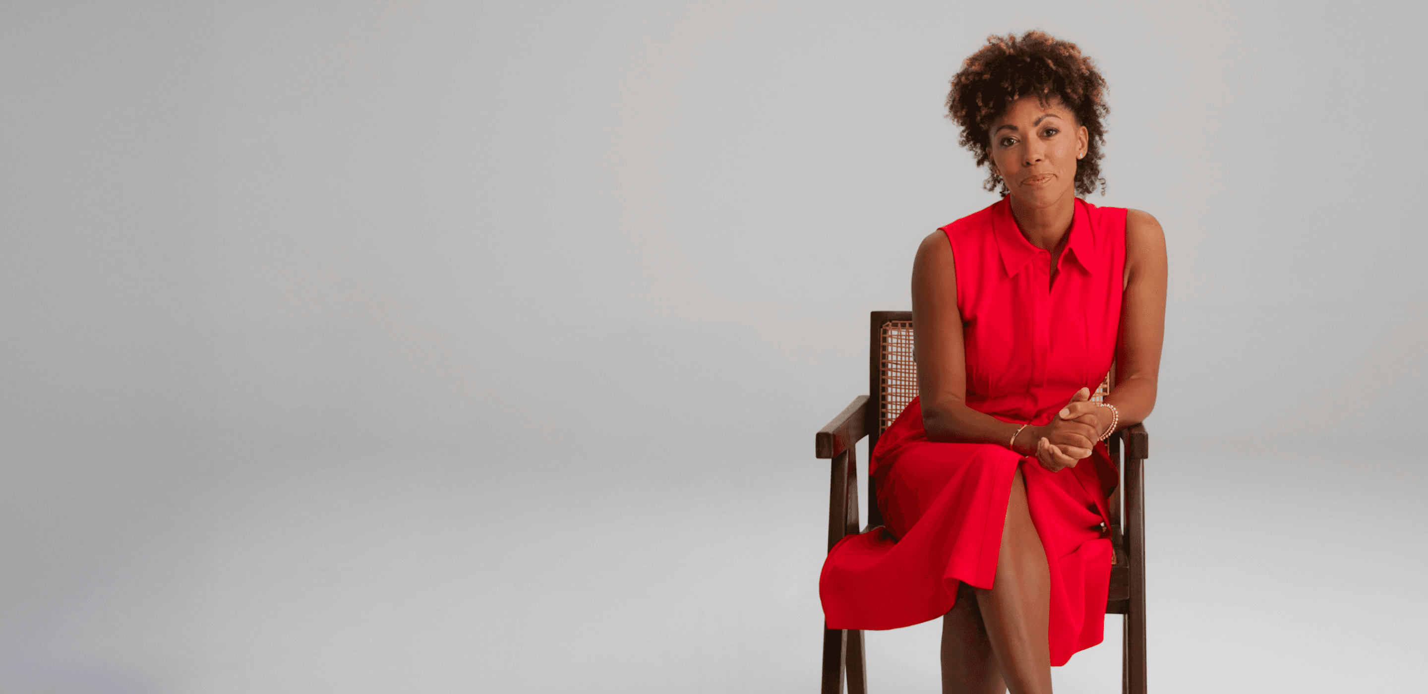 Dr Zoe Williams seated, wearing a bright red dress, and looking at the camera elegantly. 