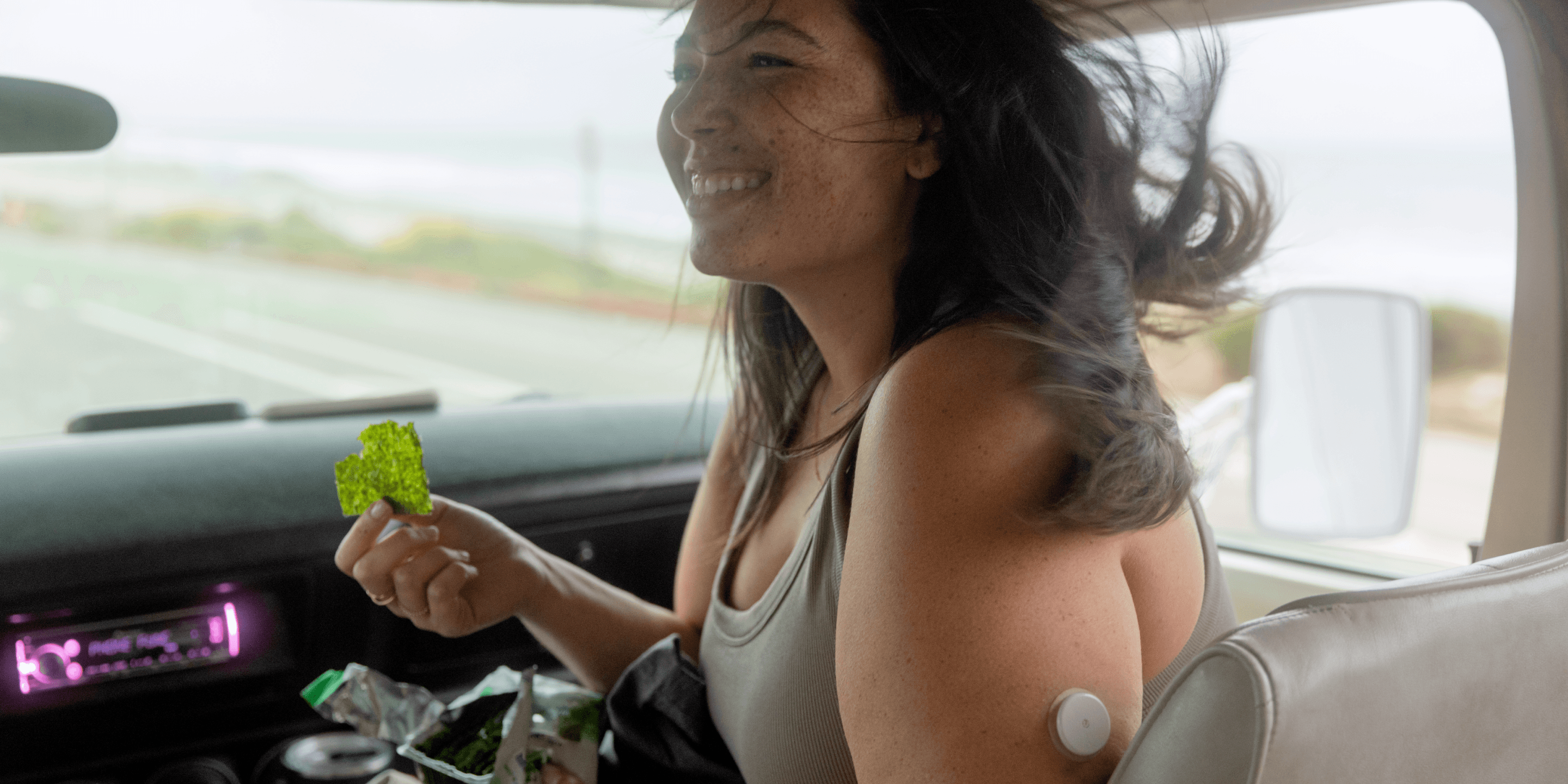 Woman in a car wearing a CGM holding dried seaweed. 