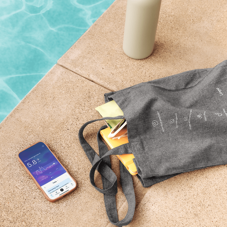 A recycled tote bag, and a phone showing the Lingo application on a pool deck next to sparkling blue water. 