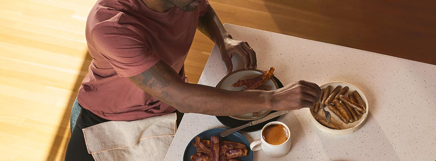 Person with coffee eating sausages and bacon