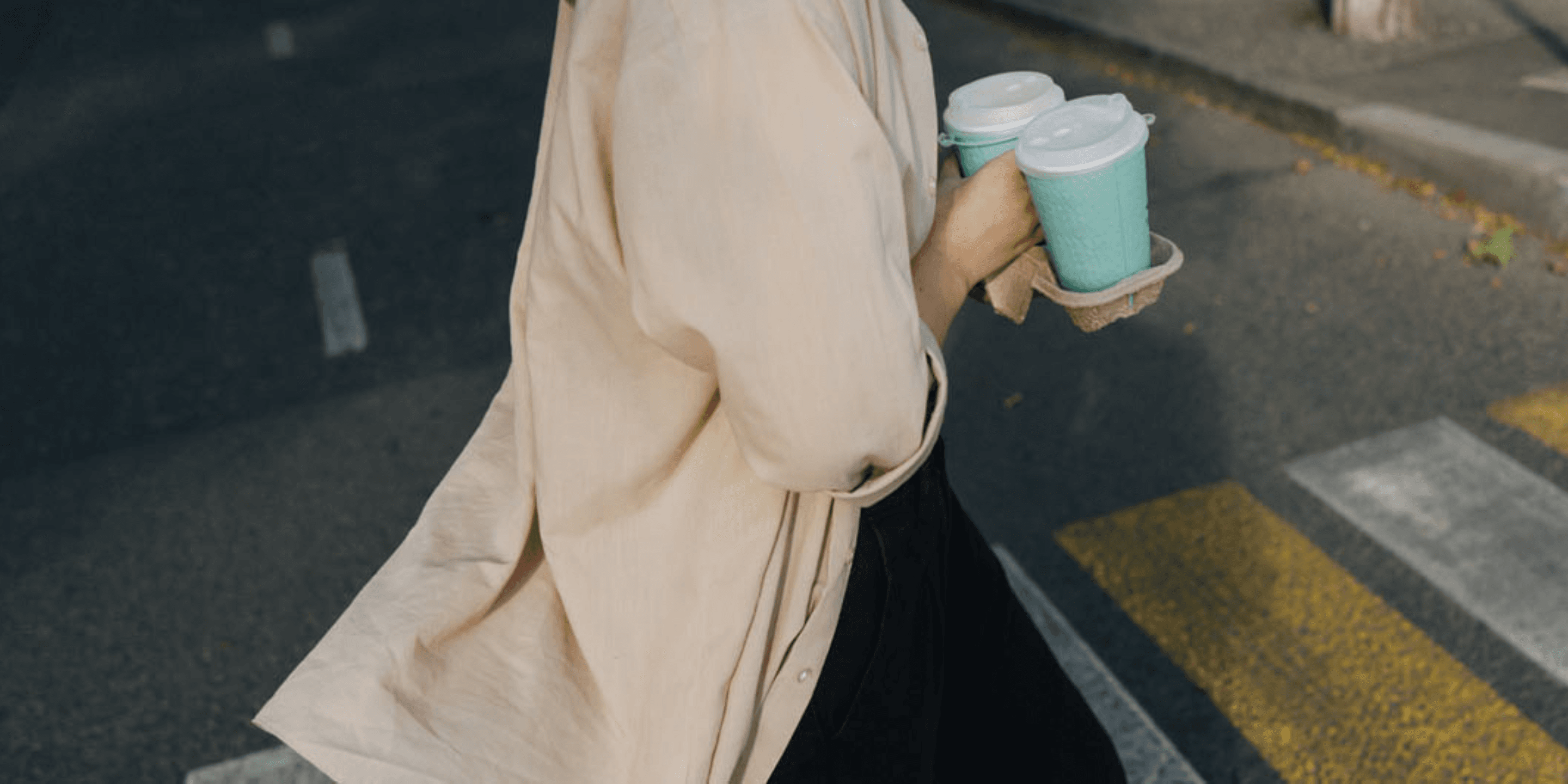 Person crossing street with two takeaway coffees 