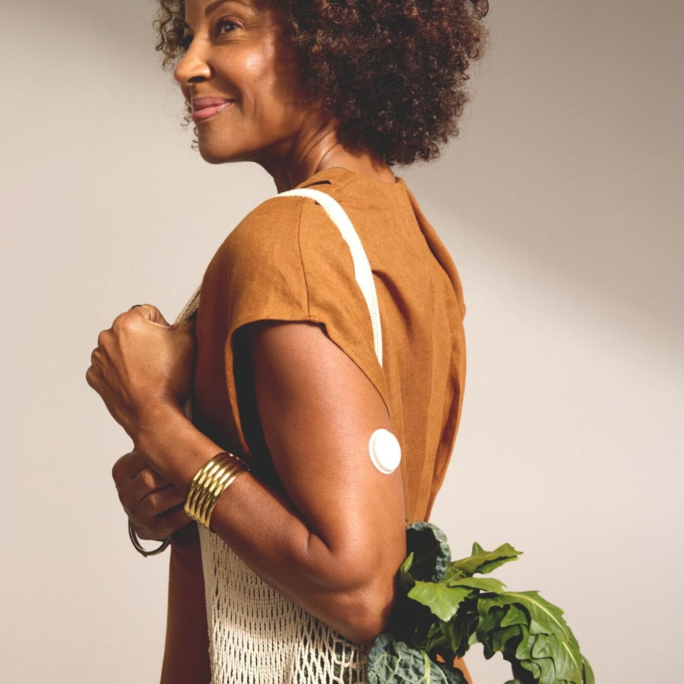 Woman wearing a CGM carrying bag of vegetables. 