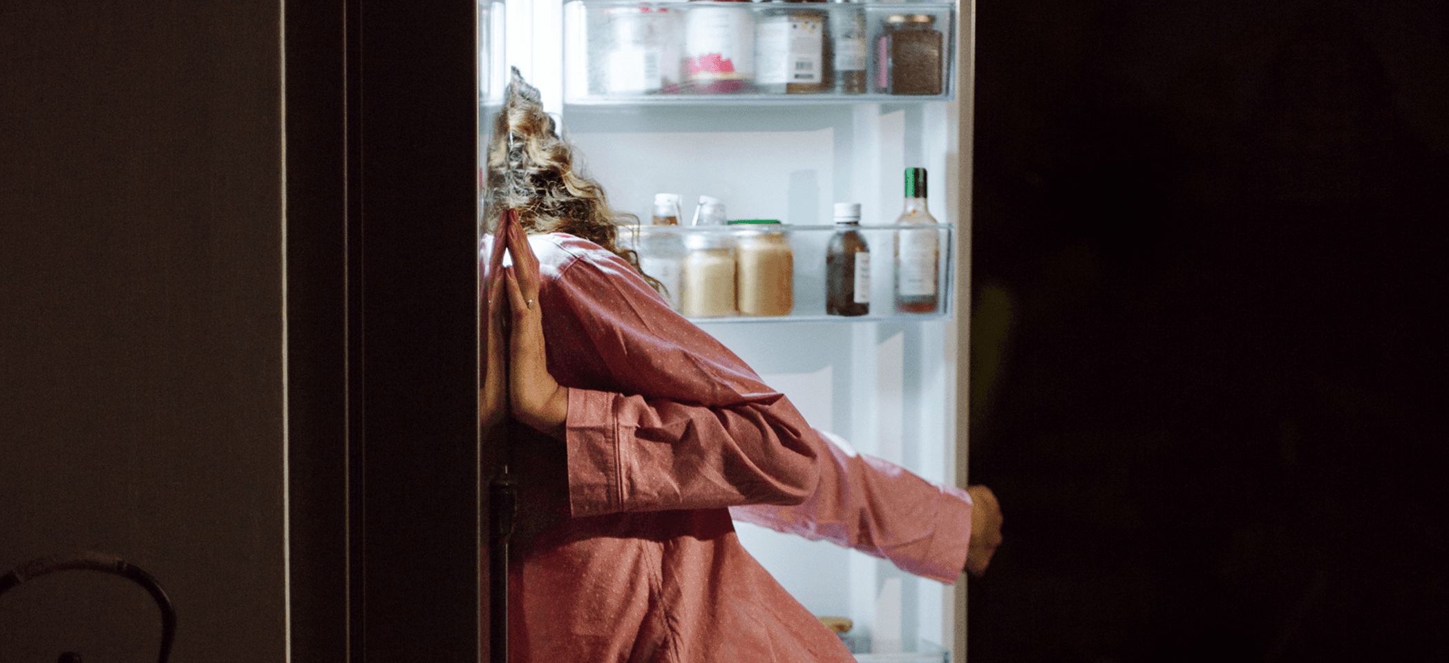 Person wearing pyjamas looking inside a fridge. 