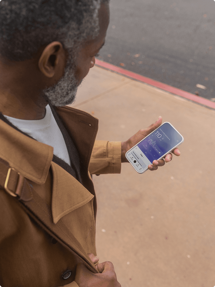 A person holding a smartphone displaying the Lingo app with a glucose reading.