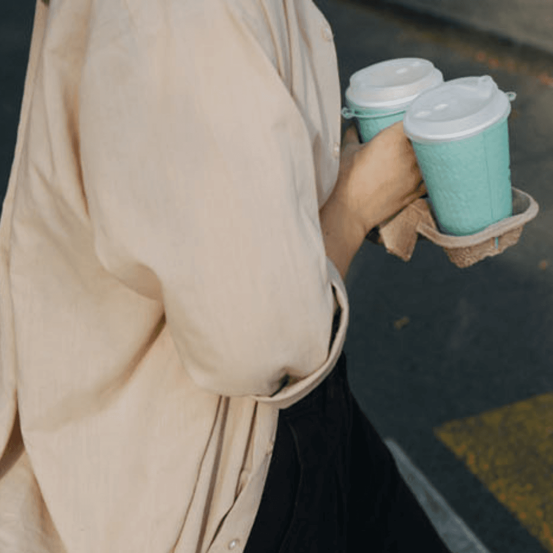 Person crossing street with two takeaway coffees