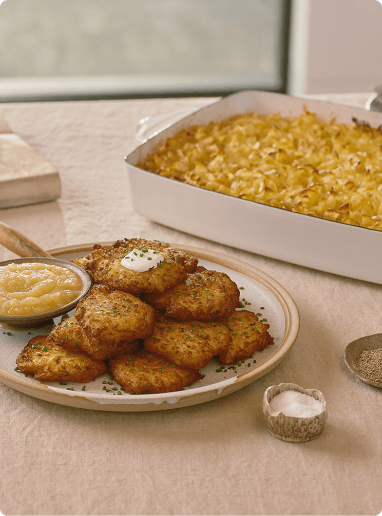 Latkes balanced on plate with a casserole of macaroni and cheese