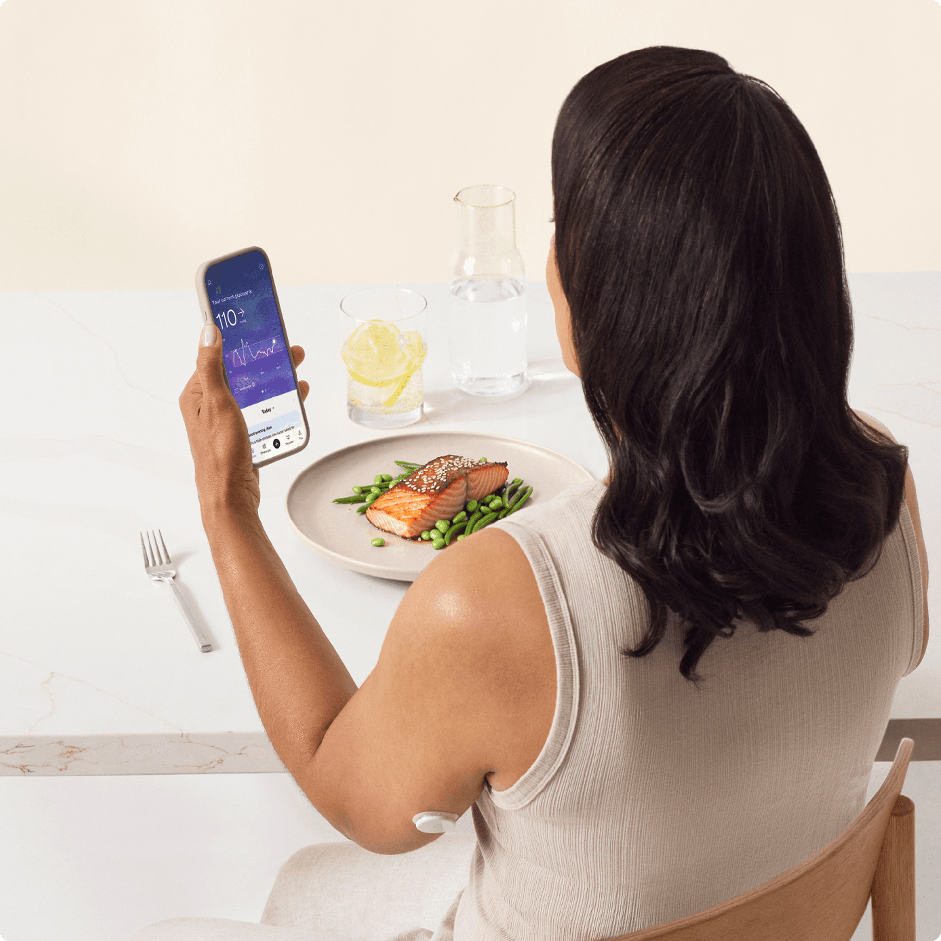 A woman sitting in a chair looking at her phone wearing a lingo biosensor