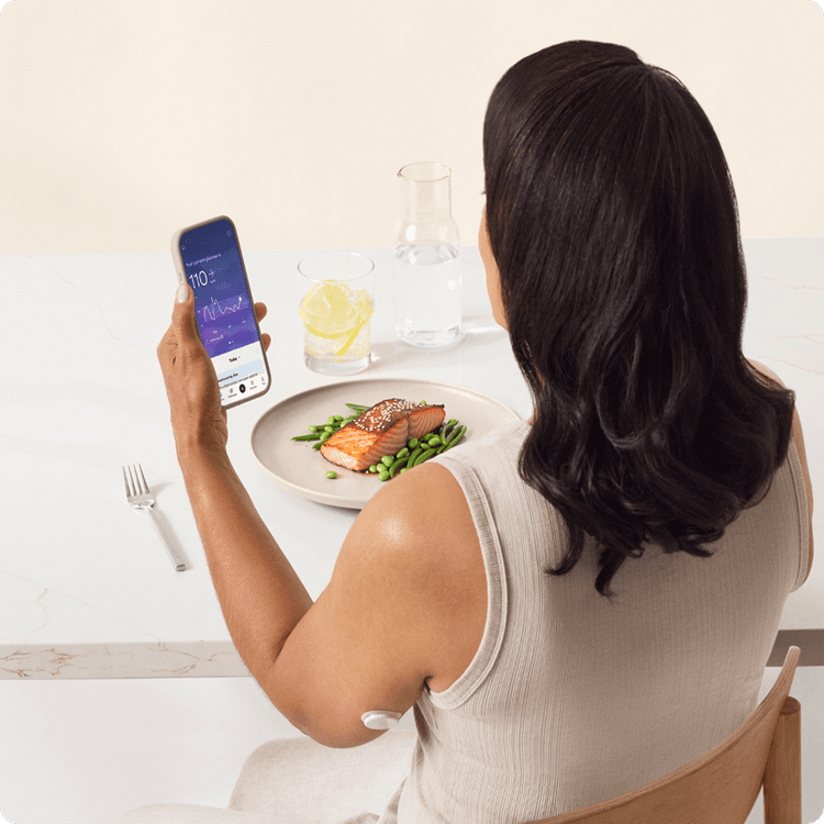 A woman sitting in a chair looking at her phone wearing a lingo biosensor