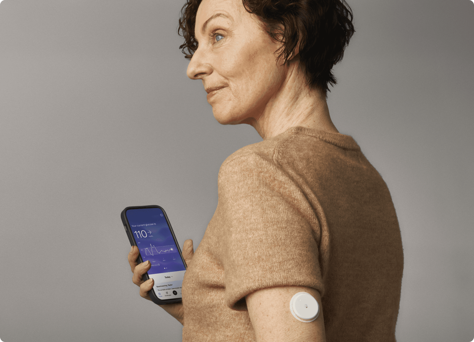 A woman wearing a CGM while holding her phone