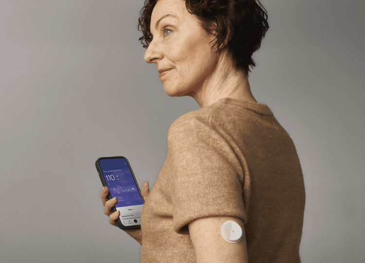 A woman wearing a CGM while holding her phone
