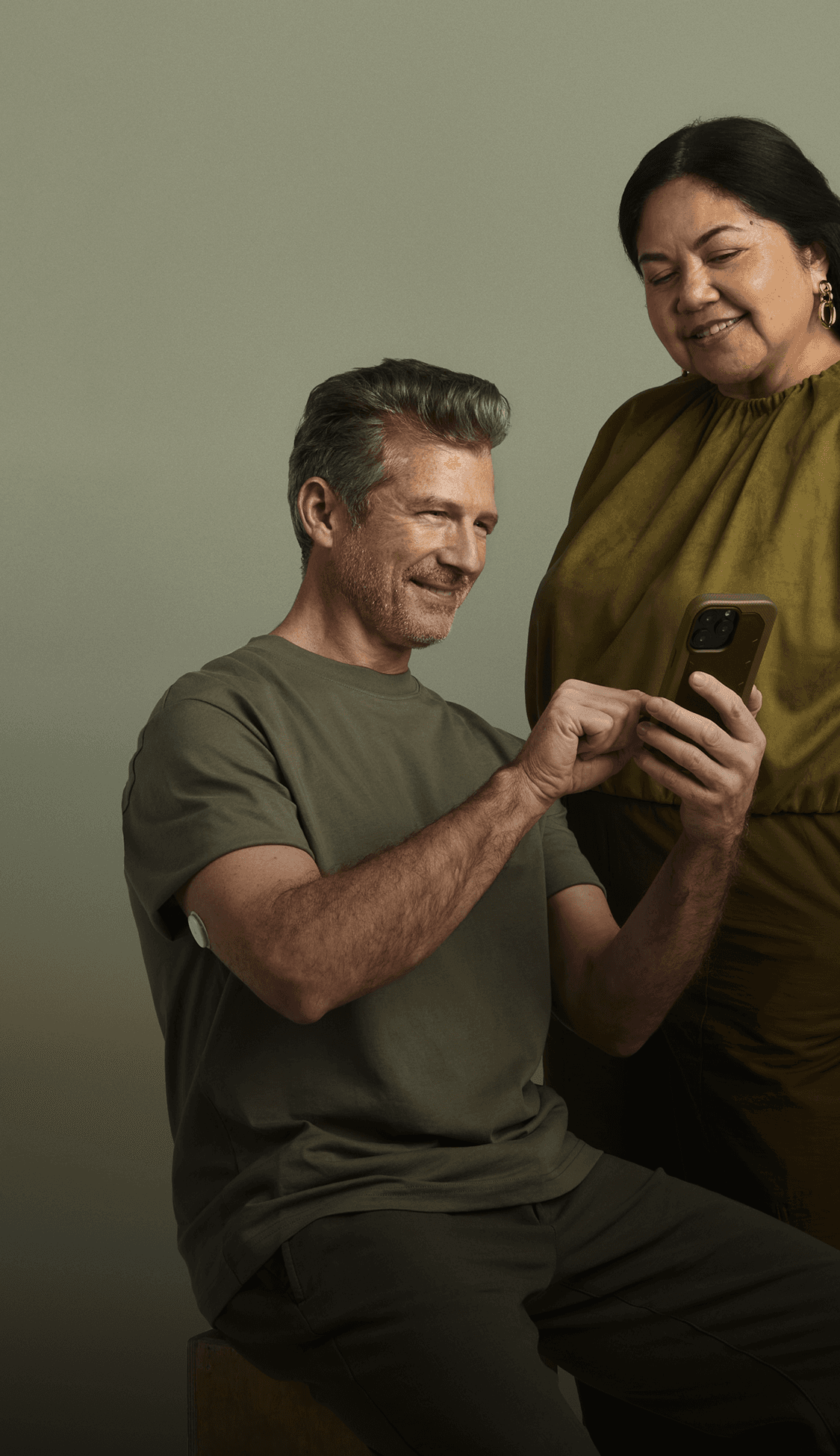 A man sitting looking at his phone and a woman looking over his shoulder