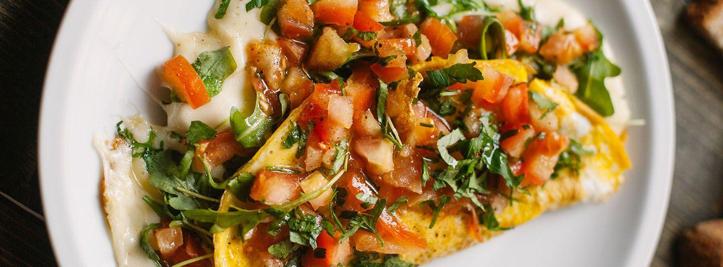 A folded omelette topped with diced tomatoes, chopped herbs, and greens.