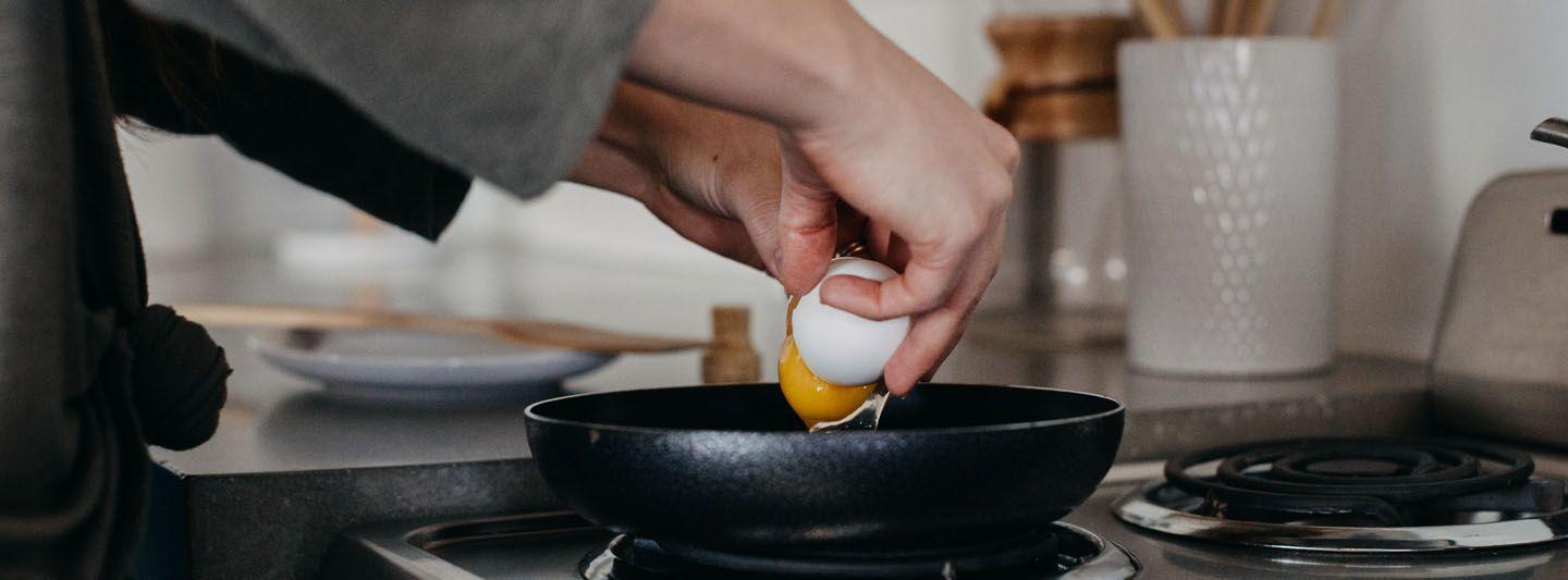 Person cracking an egg into a pan