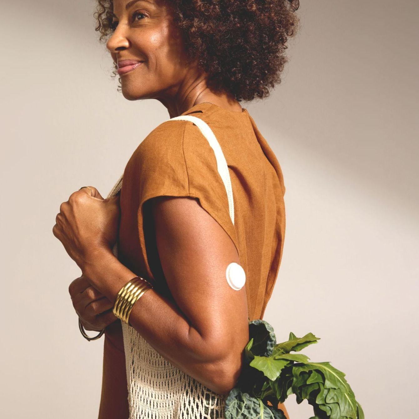 Woman wearing a CGM carrying bag of vegetables.