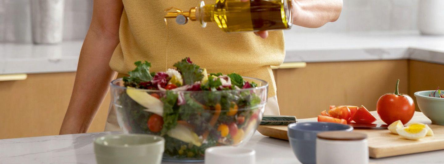 Person adding olive oil dressing to a bowl of salad