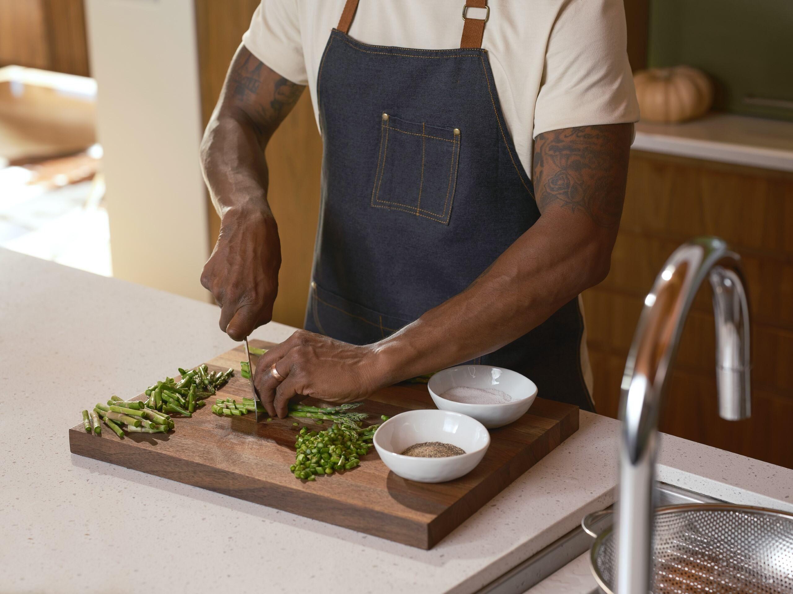 Man wearing apron chopping asparagus