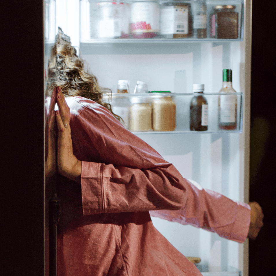 Person wearing pajamas looking inside a fridge.