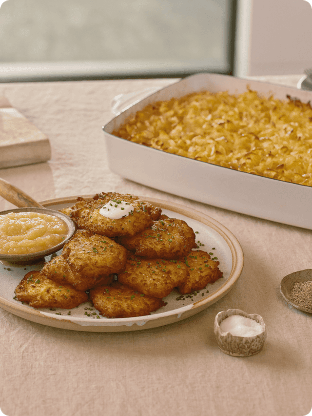 Latkes balanced on plate with a casserole of macaroni and cheese