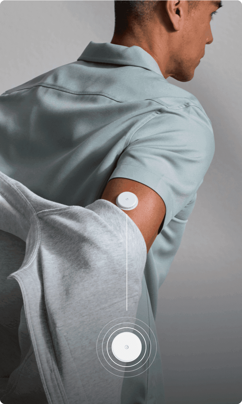 A man in a pale green shirt removing a grey jacket, with a Lingo biosensor on his arm