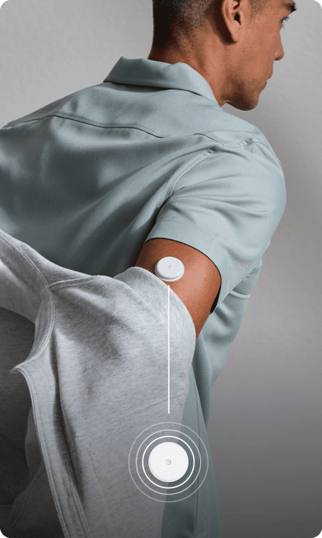 A man in a pale green shirt removing a grey jacket, with a Lingo biosensor on his arm