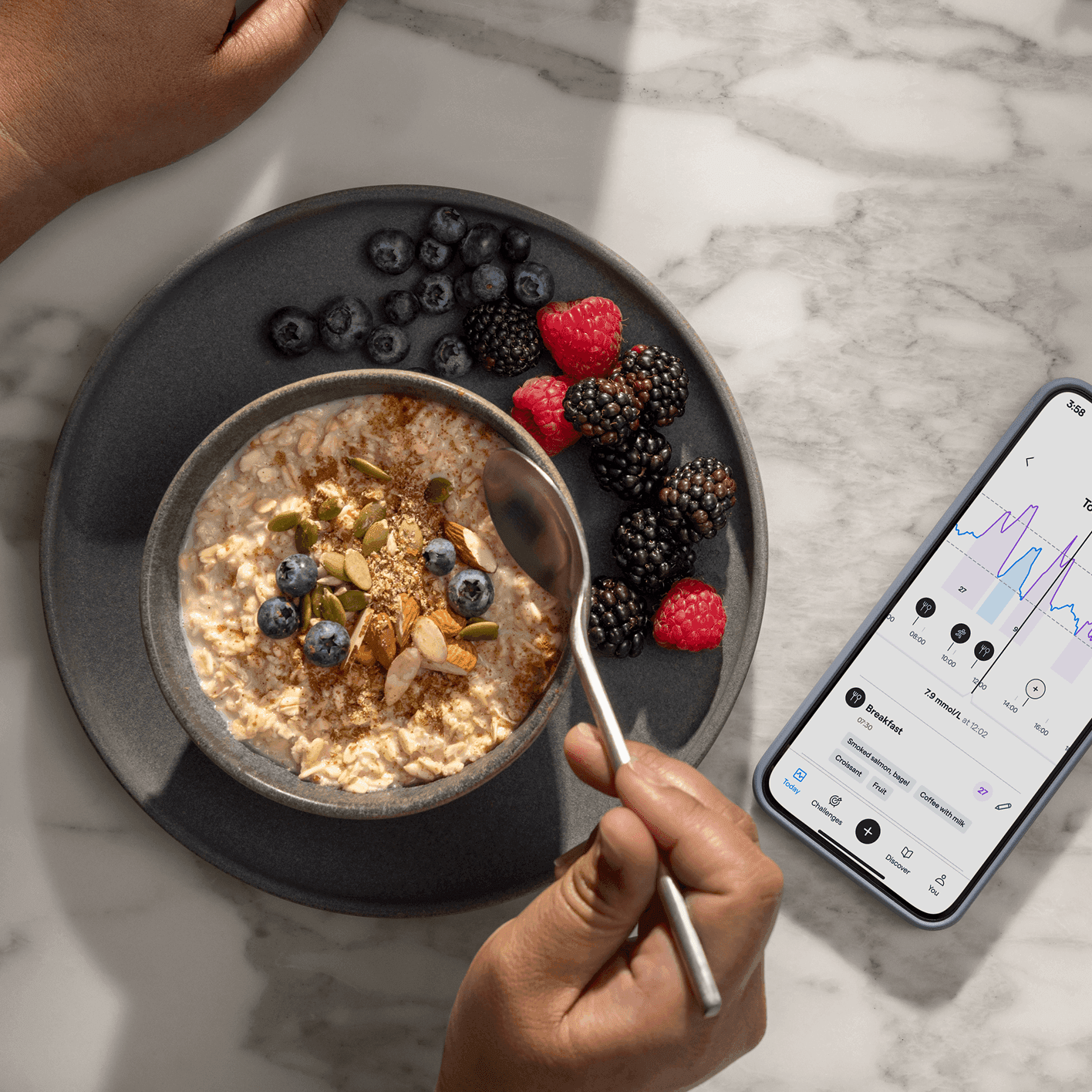A person holds a spoon over a bowl of oatmeal topped with berries and seeds, next to a smartphone showing the Lingo app.