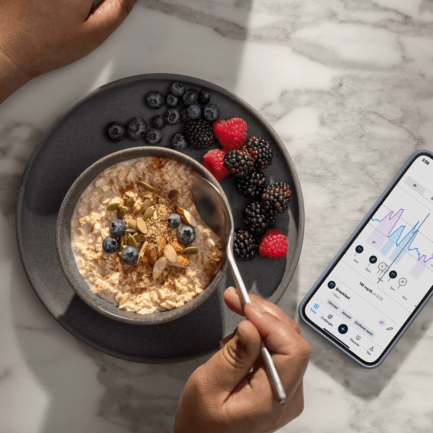 A person holds a spoon over a bowl of oatmeal topped with berries and seeds, next to a smartphone showing the Lingo app.