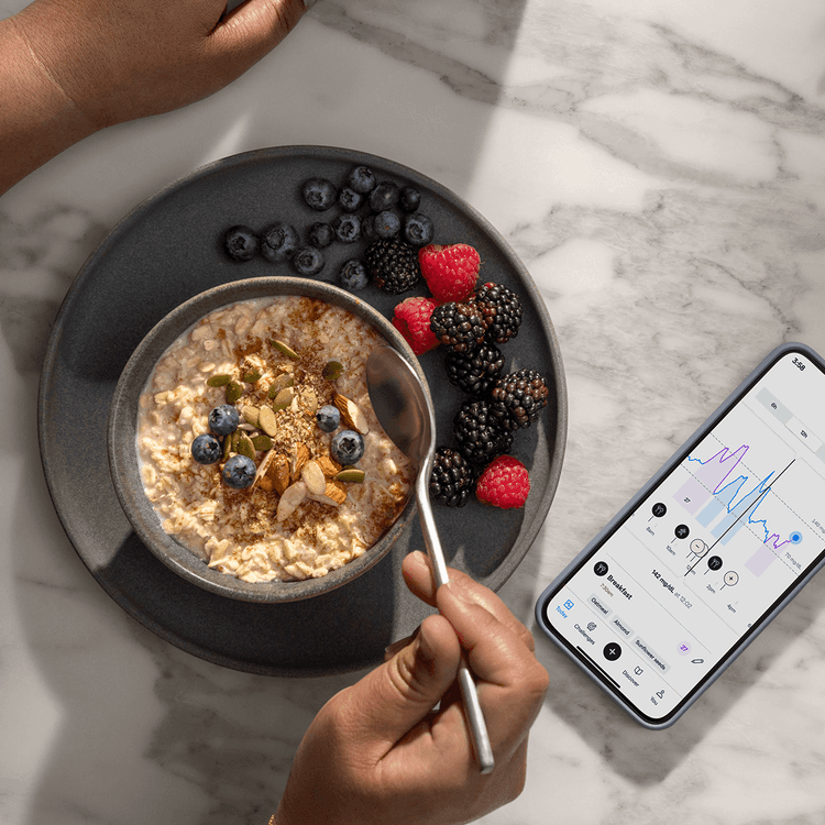 A person holds a spoon over a bowl of oatmeal topped with berries and seeds, next to a smartphone showing the Lingo app.
